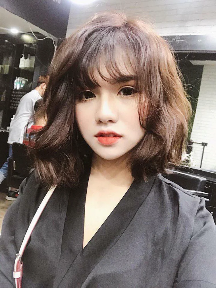 Cô gái với mái tóc xoăn ngắn màu nâu, uốn gợn nhẹ ôm gương mặt