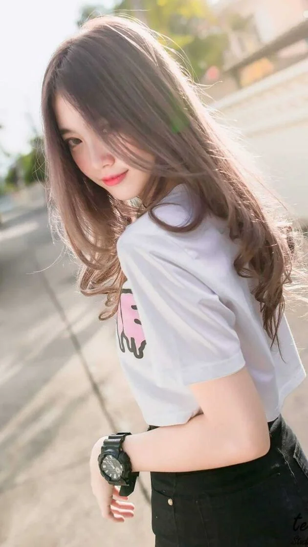 Ảnh gái xinh mặc áo croptop trắng và quần short jean ngồi trên ghế đá nhìn điện thoại trong công viên